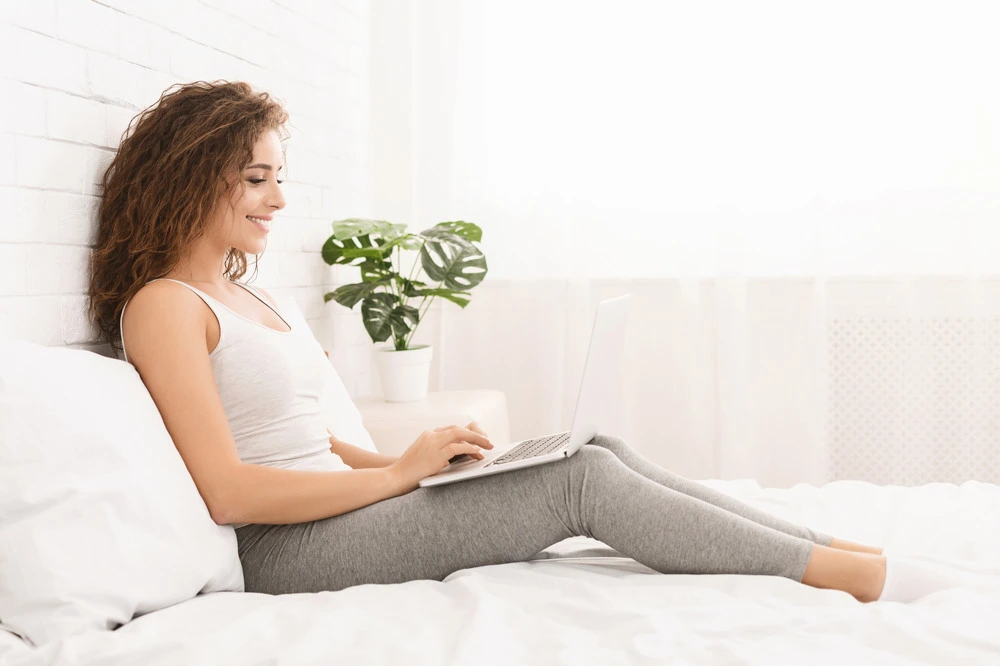girl smiling lying on the bed at home and working on a laptop