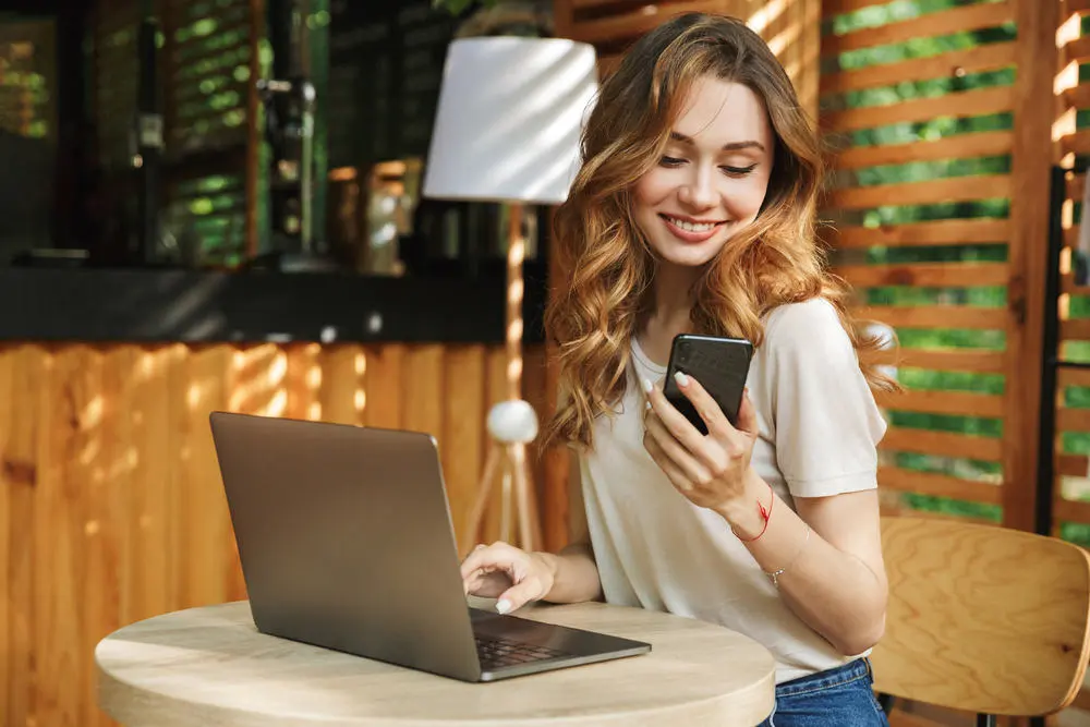 portrait of a girl smiling while looking at her phone while working on a laptop